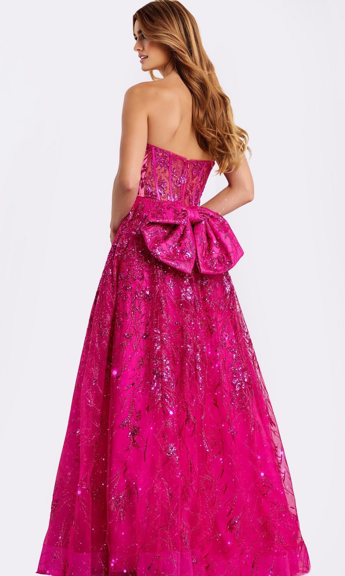 Woman facing away in the Jovani 45913 Long Prom Dress—a strapless, floor-length bright pink gown with a corset bodice, glitter details, and a large bow at the back.